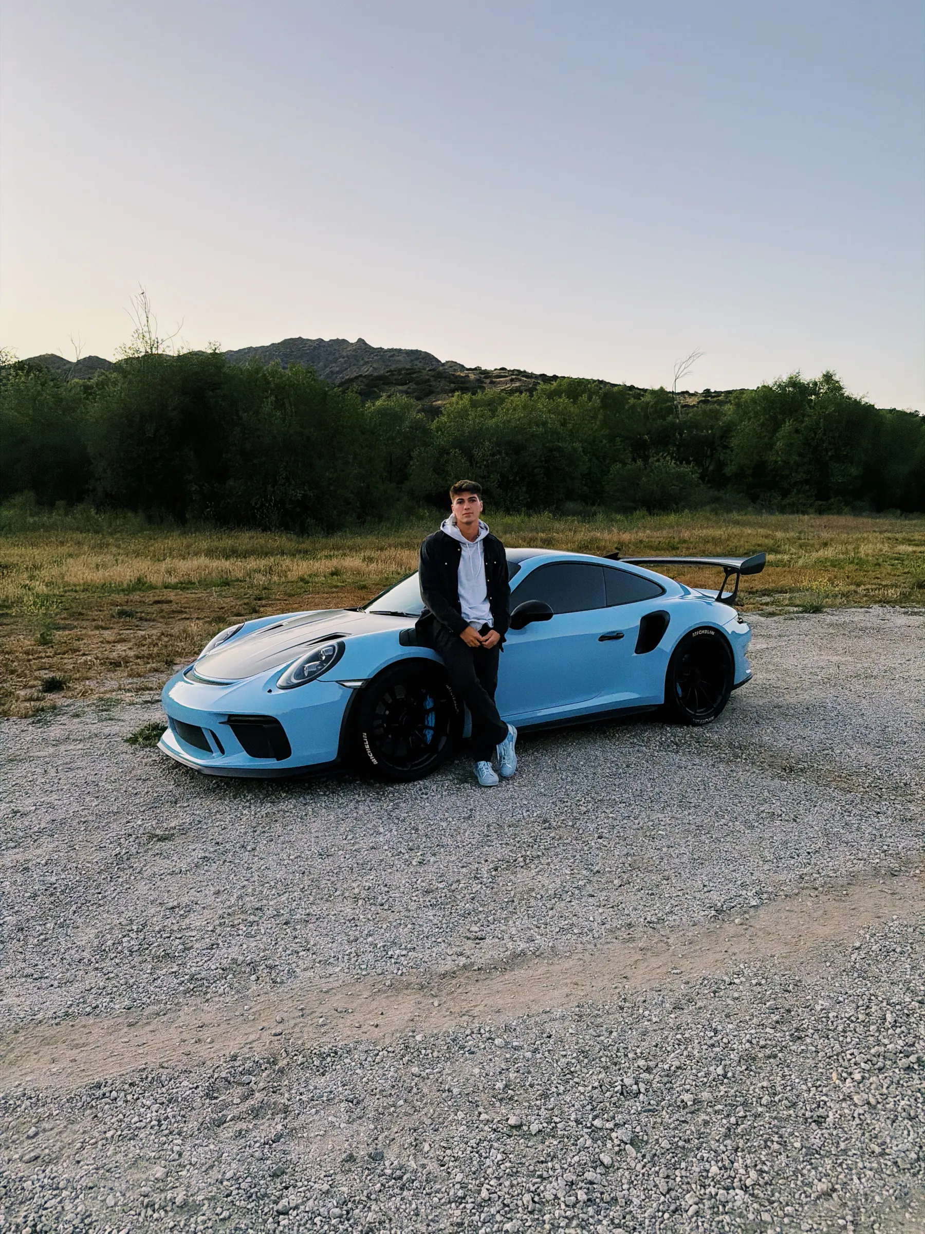Thomas leaning on a blue Porsche 911 GT3 RS in a field